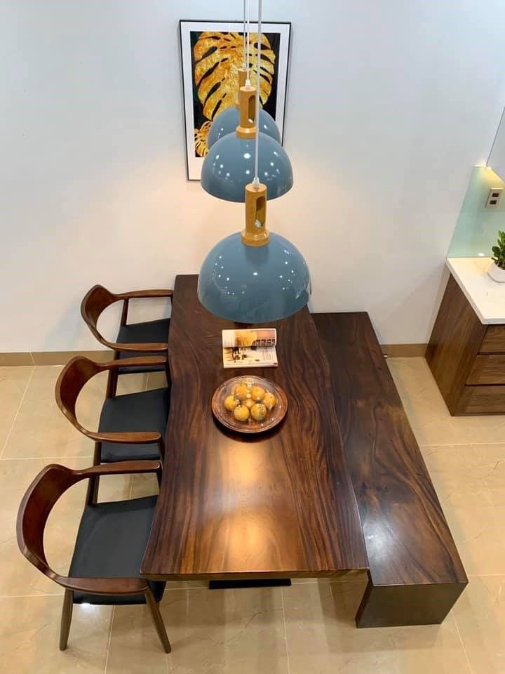 Một chiếc bàn ăn gỗ nguyên khối ngăn cách phòng khách bếp trang trí bằng tranh và đèn