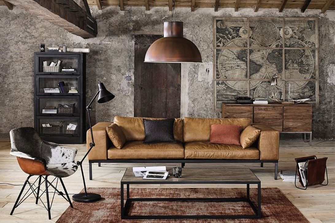 Một góc phòng khách phong cách Industrial với bức tường bê tông mài và ghế sofa da màu nâu.